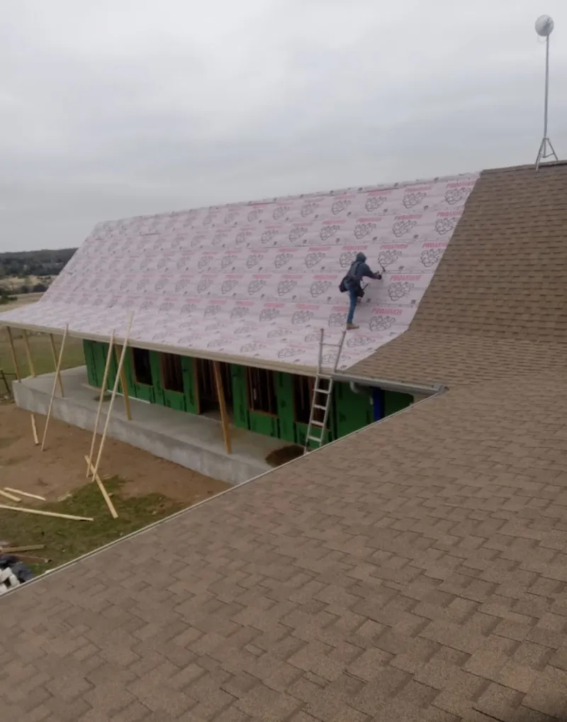 Worker preparing underlayment for a metal roof installation in West Jefferson